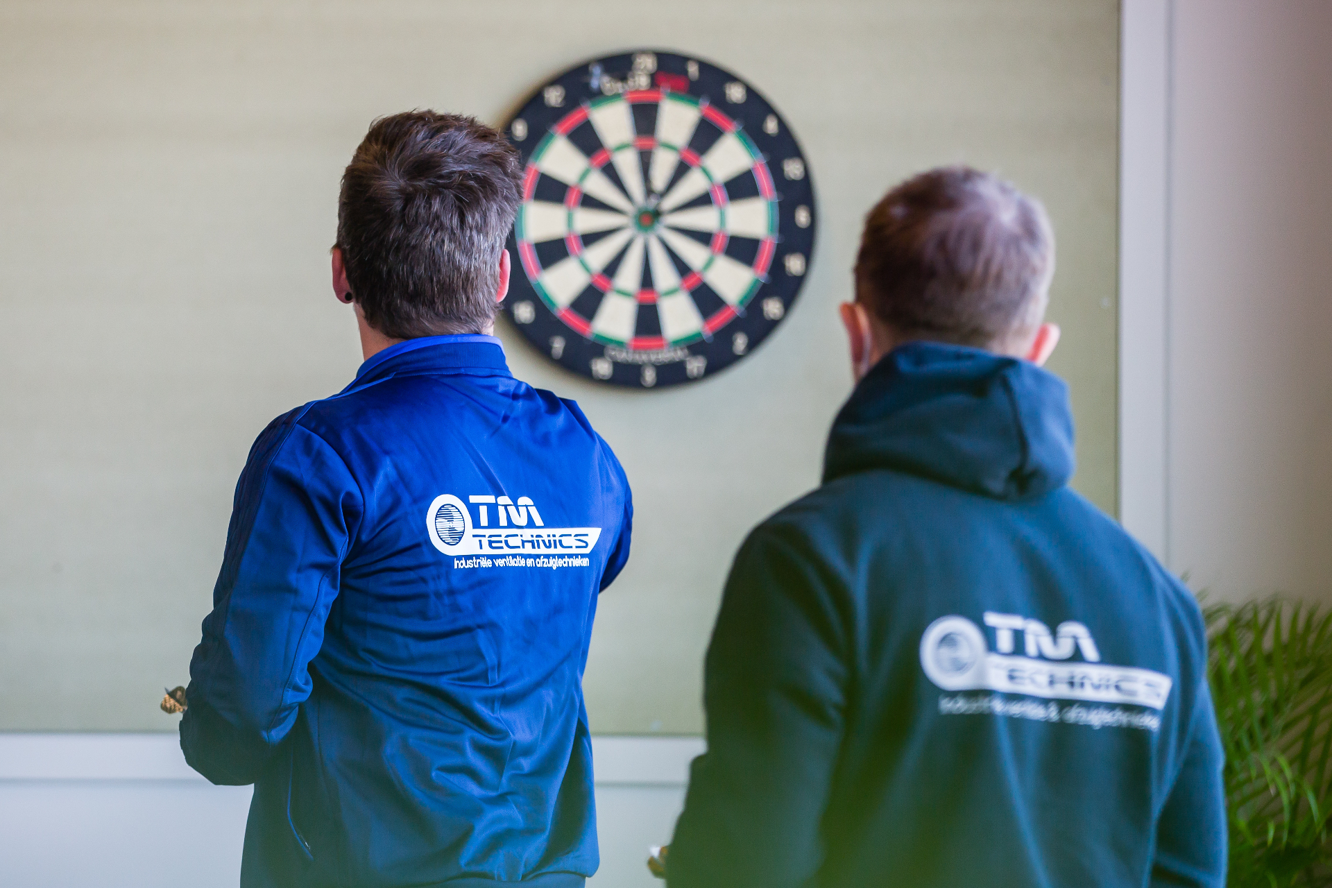 Twee luchTMeesters in TM Technics werkkledij bij een dartsbord